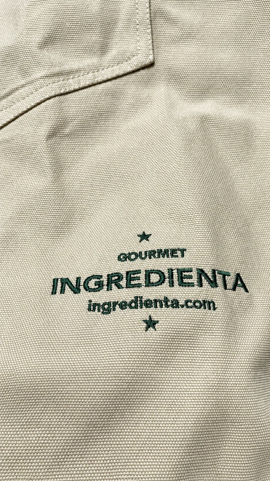 Bordado verde de Ingredienta sobre tela clara, con textura de hilo visible.